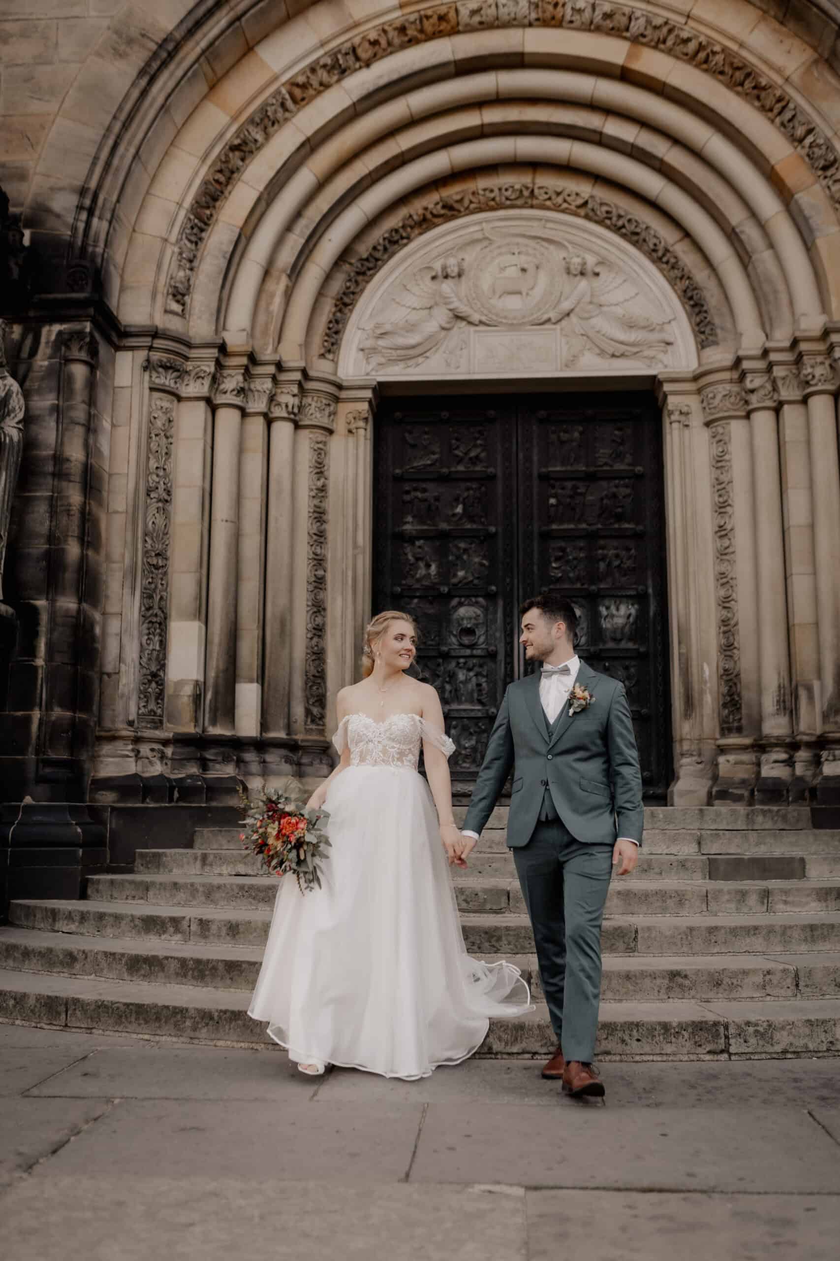 Braut und Bräutigam vor einer historischen Kirche bei ihrer Hochzeit.
