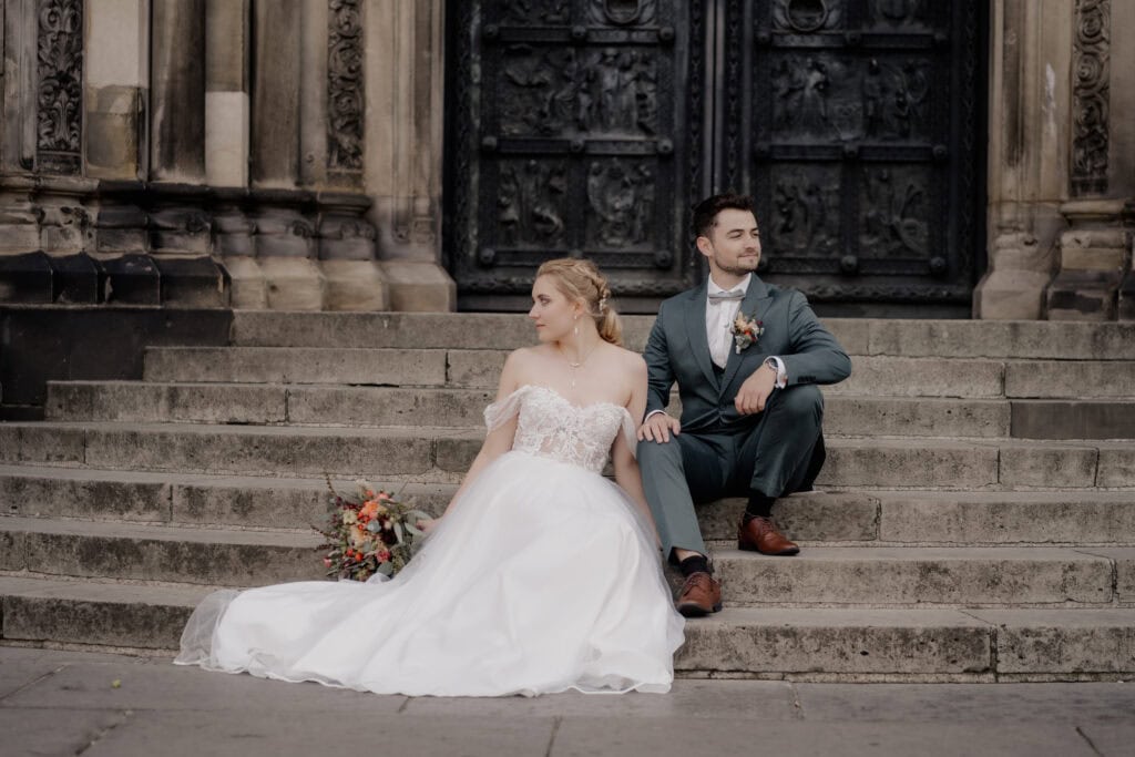 Braut und Bräutigam sitzen auf Treppe vor altem Gebäude bei Hochzeit.