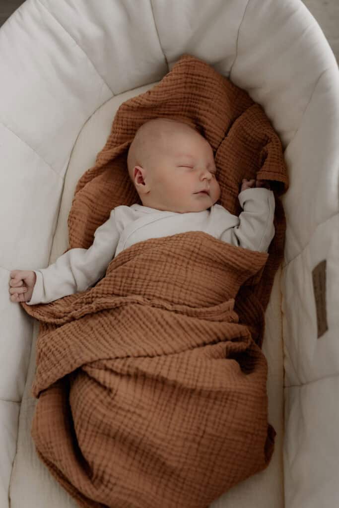 Kleines Baby schläft friedlich in einem Bett mit braunem Tuch.