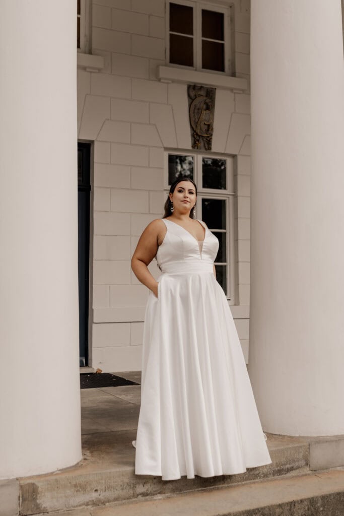 Braut in weißem Hochzeitskleid vor historischen Gebäudespalten.