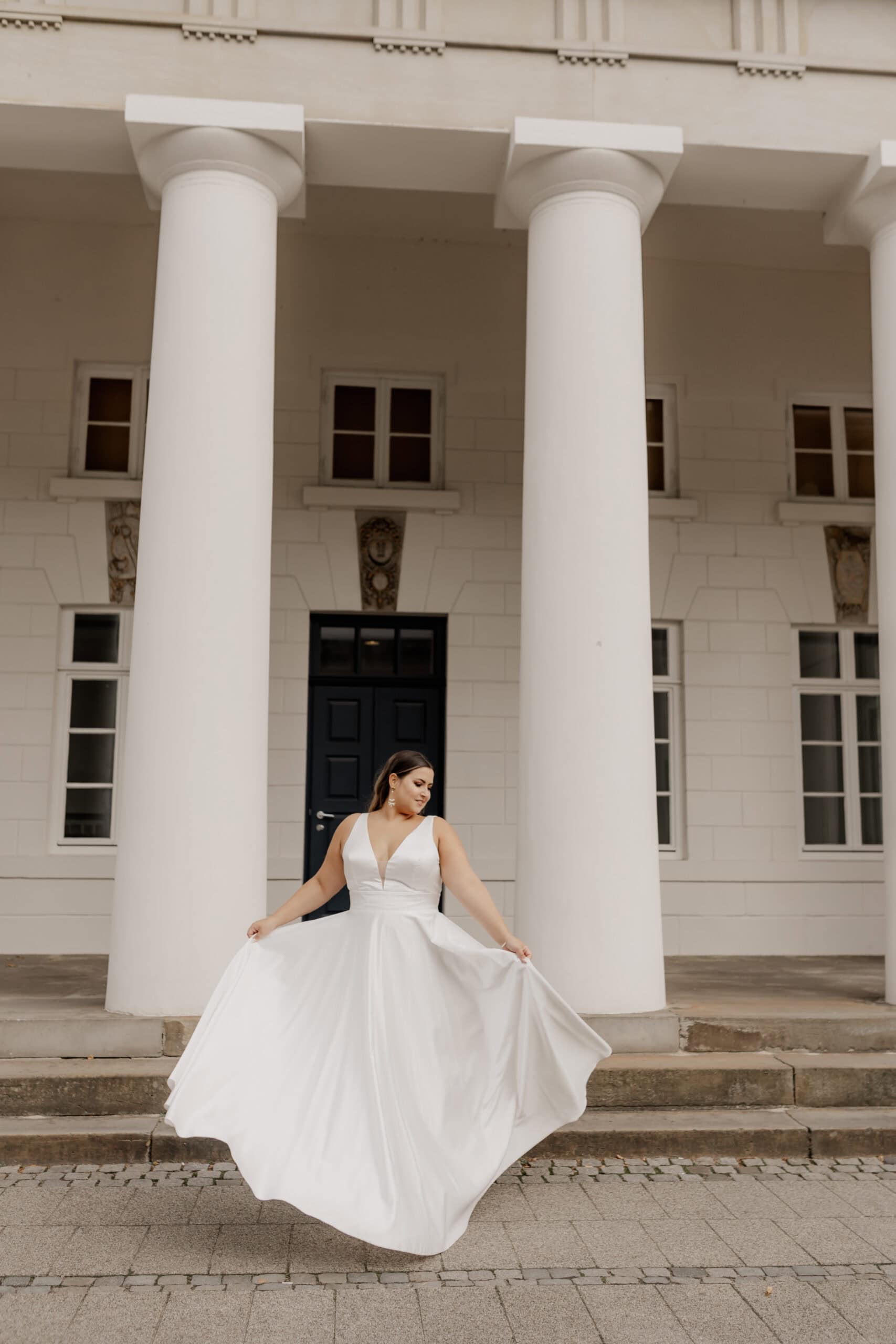 Braut in weißem Kleid vor klassischer Säulenfassade.