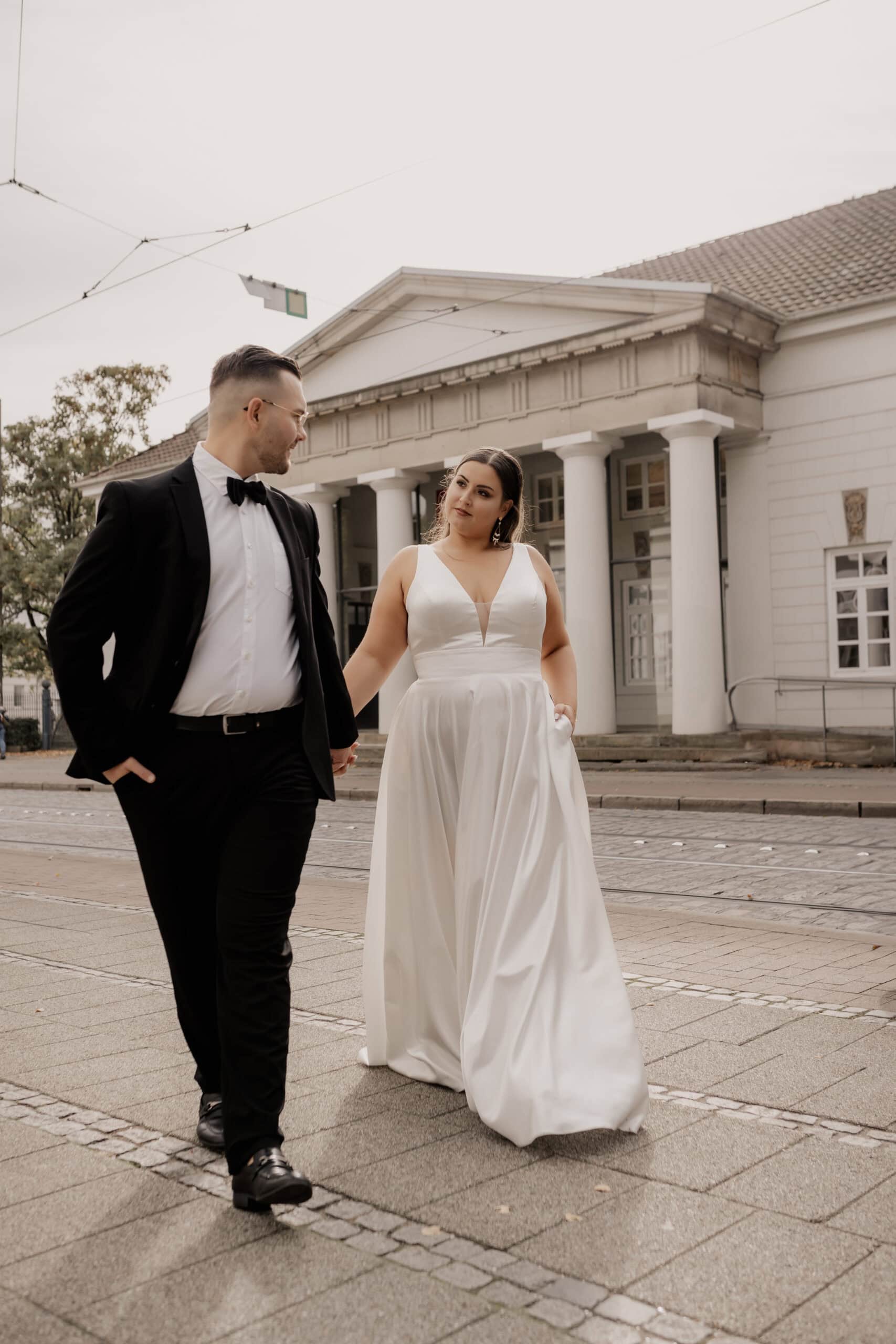 Brautpaar in eleganter Hochzeitskleidung vor historischem Gebäude.