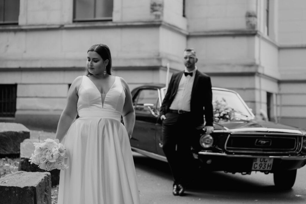 Braut mit Blumenstrauß vor einem klassischen Auto bei Hochzeitsfotoshooting.
