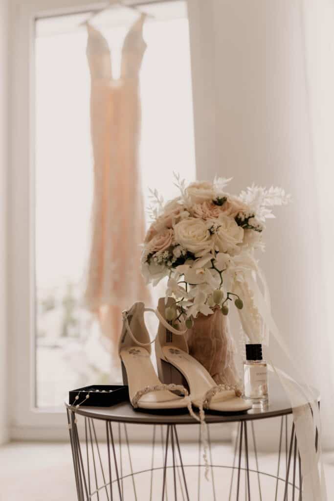 Brautschuhe, Brautstrauß und Hochzeitskleid im Hintergrund.
