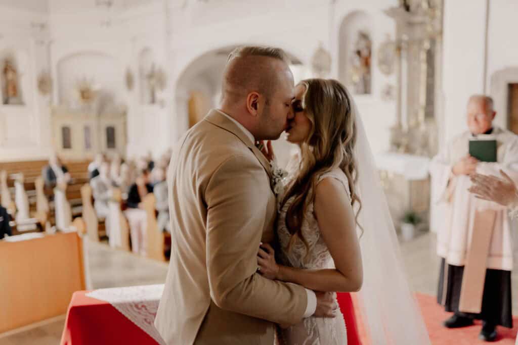 Braut und Bräutigam küssen sich bei Hochzeit in Kirche.