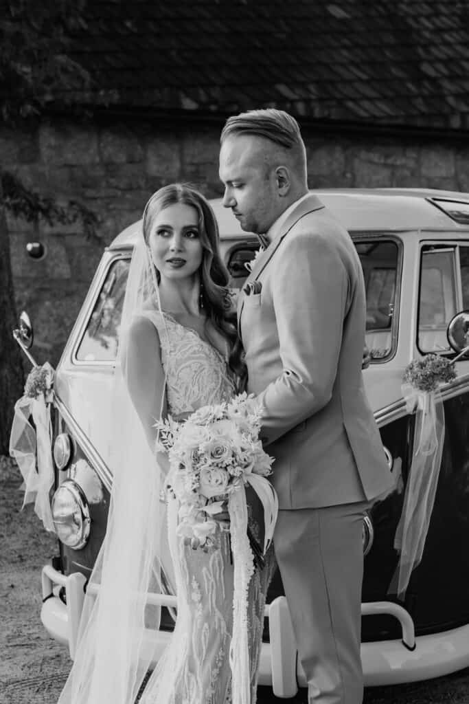 Braut und Bräutigam vor einem Vintage-Auto bei ihrer Hochzeit.