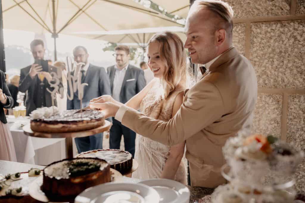 Brautpaar schneidet Hochzeitstorte bei einer Feier im Freien.