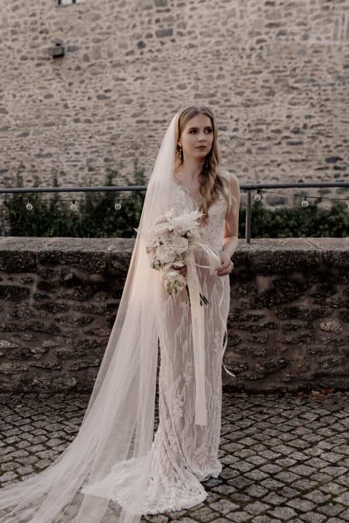 Braut Miriam Weimer in eleganter Hochzeitskleidung vor Burgmauer.