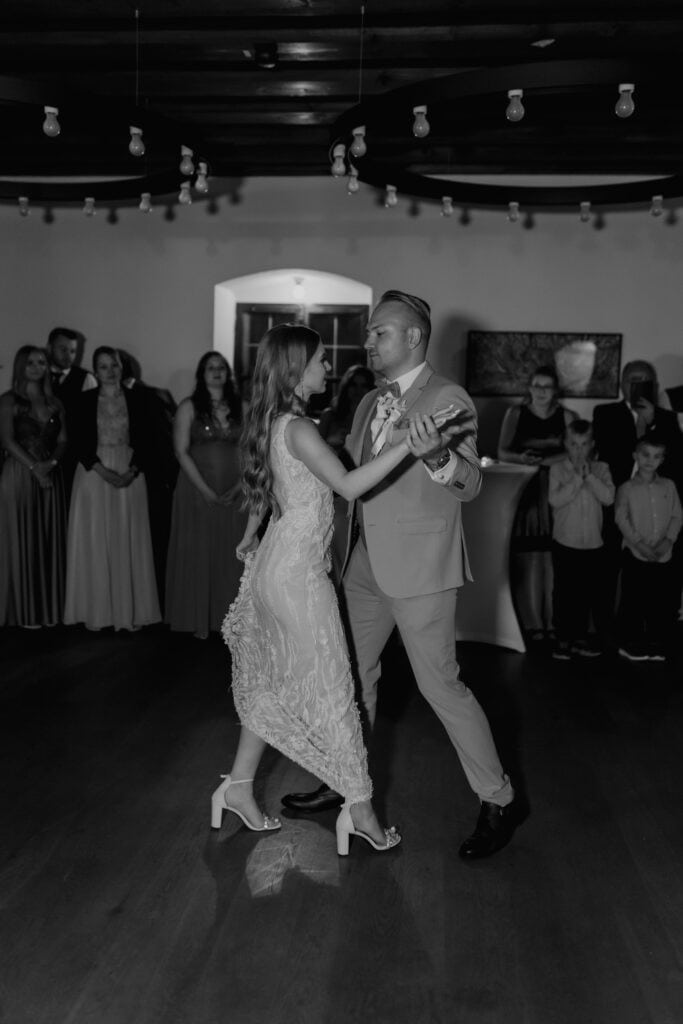 Braut und Bräutigam tanzen bei Hochzeit, Gäste im Hintergrund.