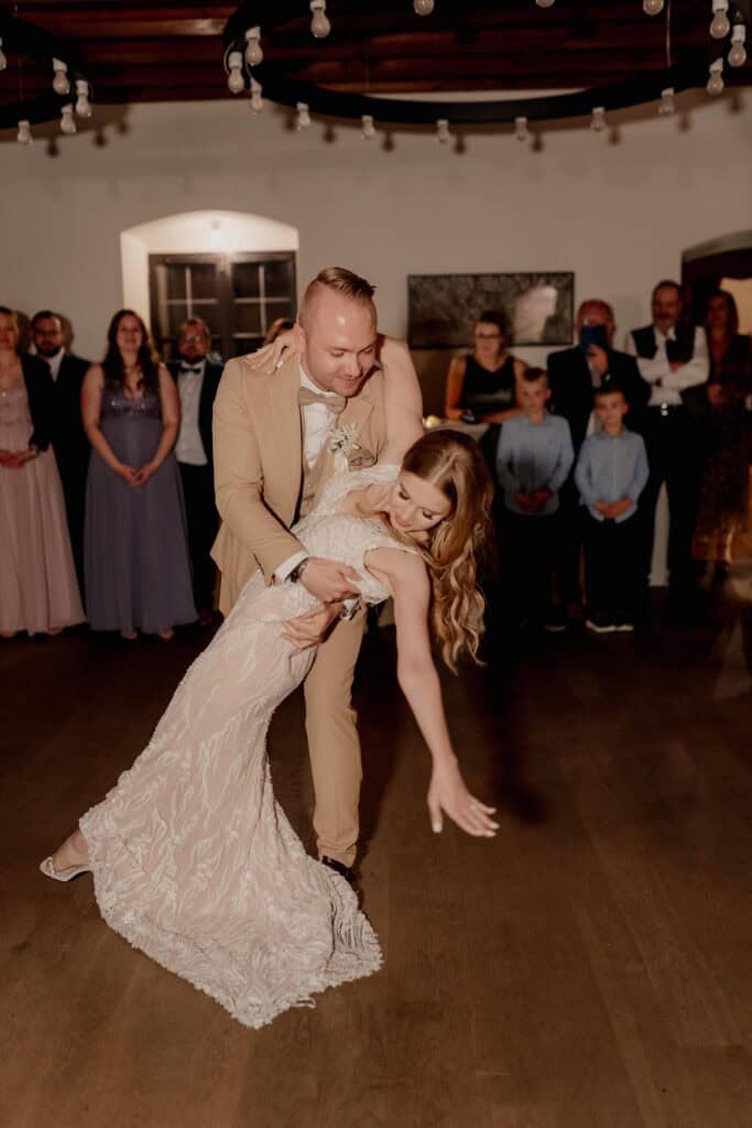 Braut und Bräutigam tanzen beim Hochzeitstanz, Gäste im Hintergrund.