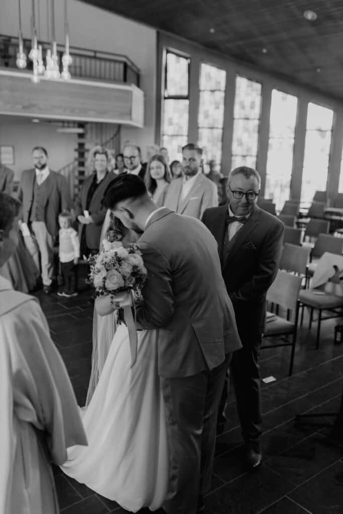 Hochzeitsszene mit Braut, Bräutigam und Gästen in moderner Kirche.