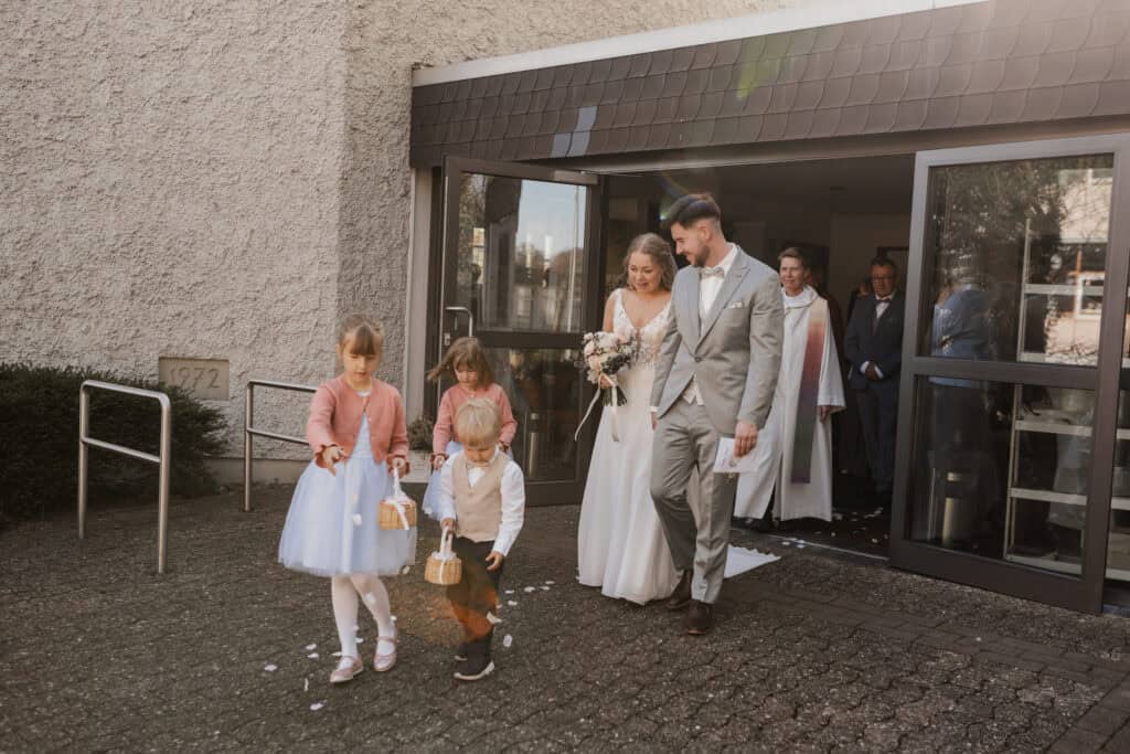 Hochzeitspaar mit Kindern vor der Kirche in eleganten Outfits.