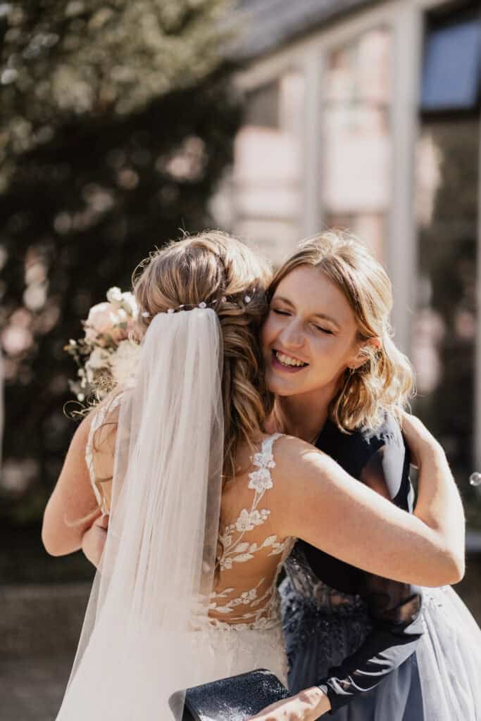 Emotionale Umarmung bei einer Hochzeit, Braut und Freundin lachen.