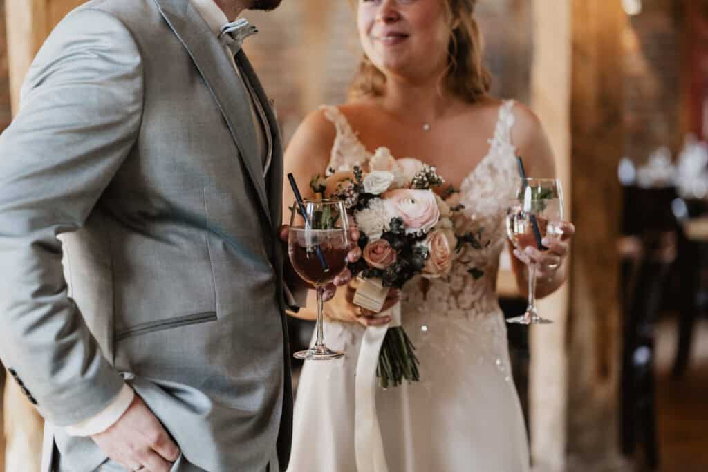 Braut und Bräutigam bei der Hochzeit mit Blumenstrauß und Weingläsern.