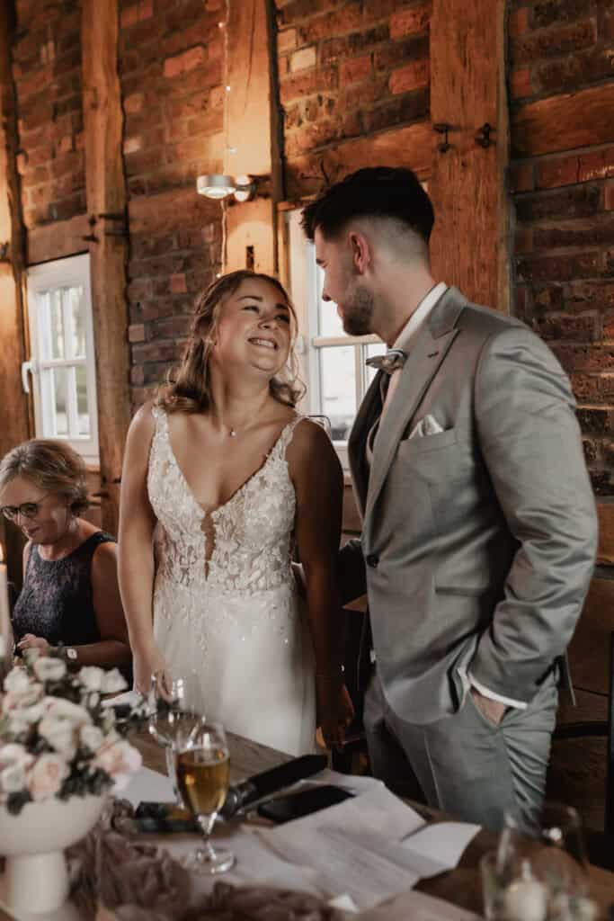Braut und Bräutigam lachen bei ihrer Hochzeit in einem rustikalen Raum.