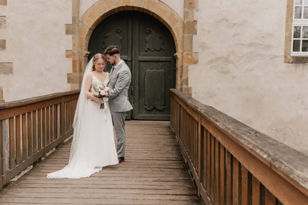 Braut und Bräutigam auf Brücke vor altem Tor bei Hochzeit.