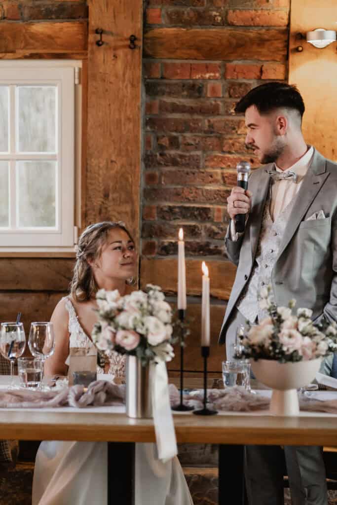 Hochzeitsszene mit Braut und Bräutigam bei Rede in rustikalem Raum.