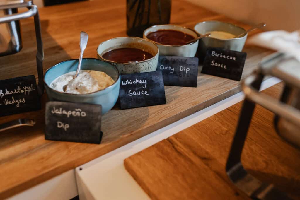 Verschiedene Saucen auf einem Buffet mit kleinen Schildern.