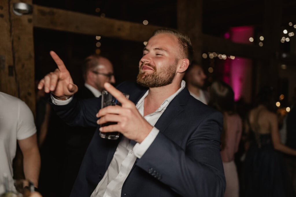 Mann beim Feiern auf einer Hochzeit, lächelnd und mit Getränk in der Hand.