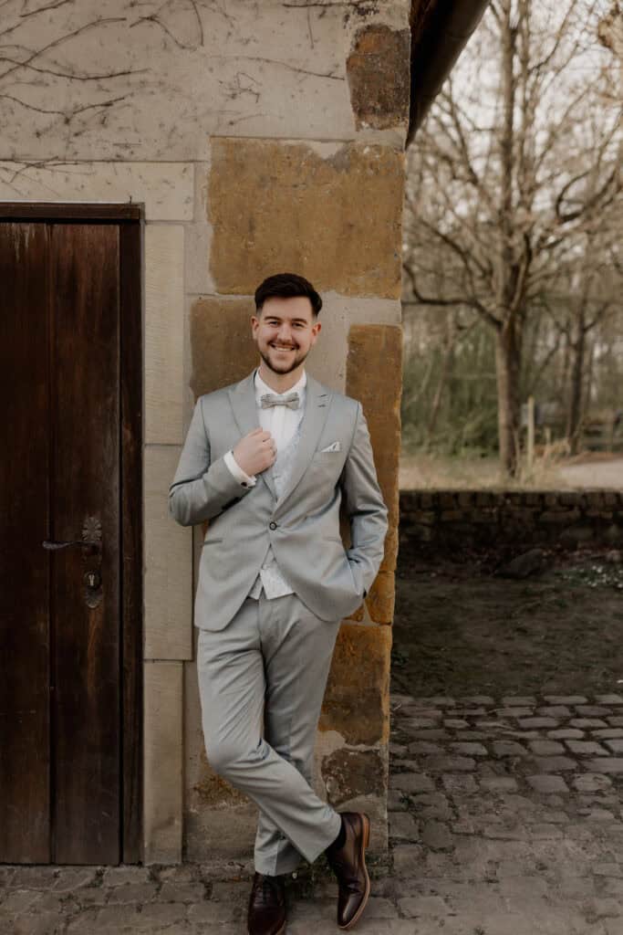 Mann in grauem Anzug vor altem Steinmauer bei Hochzeit.