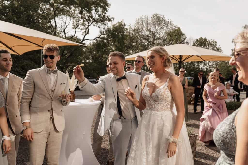 Hochzeit im Freien mit lachendem Brautpaar und Gästen bei Sonnenuntergang.