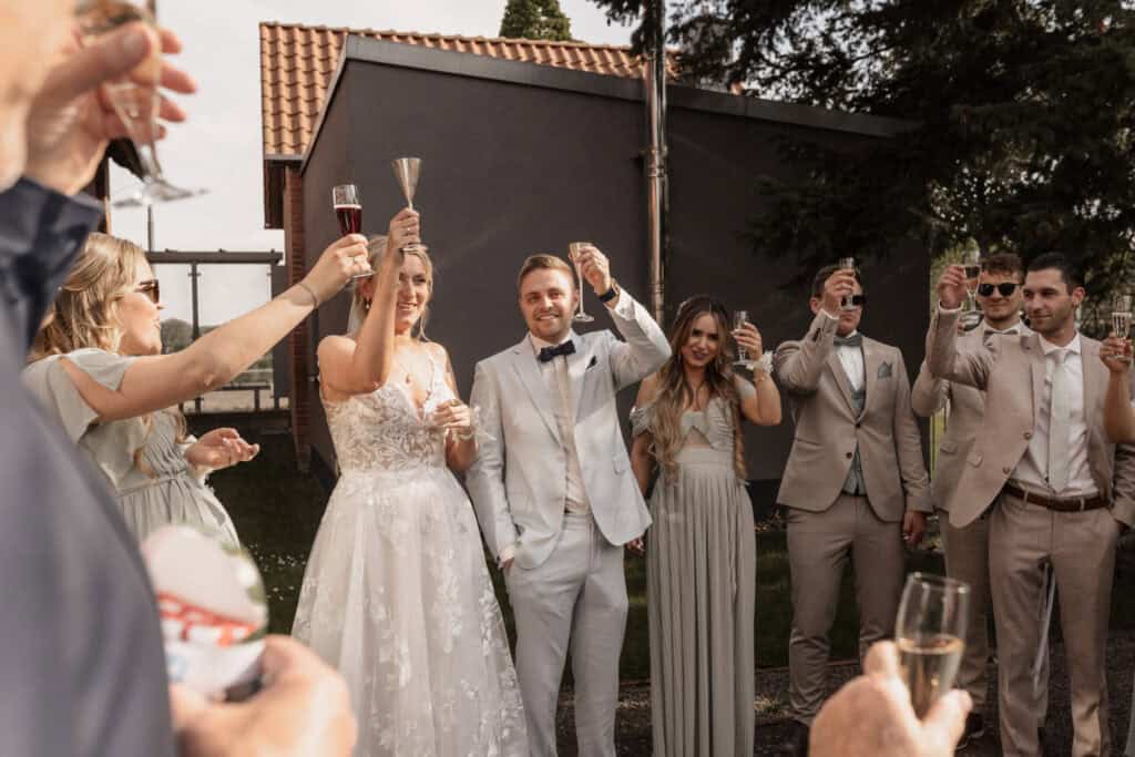Hochzeitspaar mit Freunden beim Anstoßen im Garten.