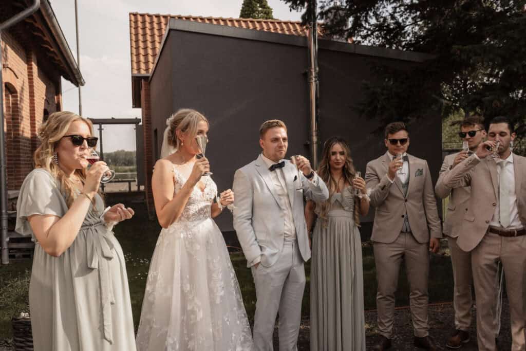Hochzeitspaar mit Freunden beim Anstoßen im Garten.