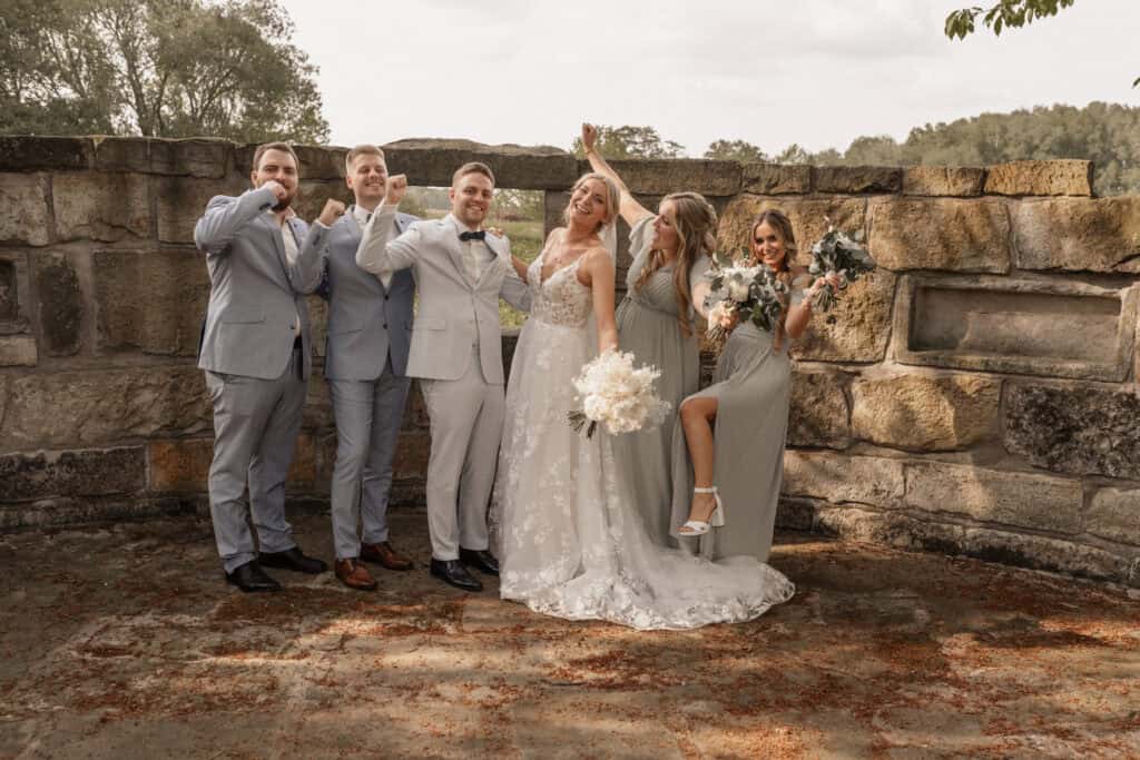 Hochzeitspaar mit Freunden vor Steinmauer in Naturkulisse.