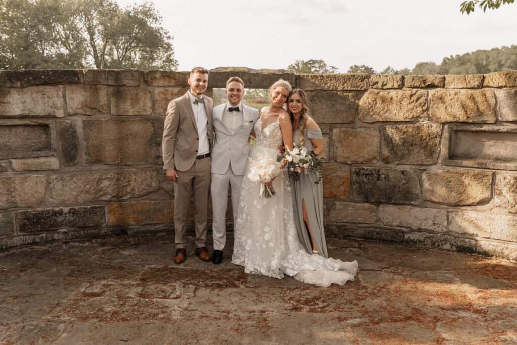 Hochzeit mit Braut, Bräutigam und Gästen vor alter Steinmauer in der Natur.