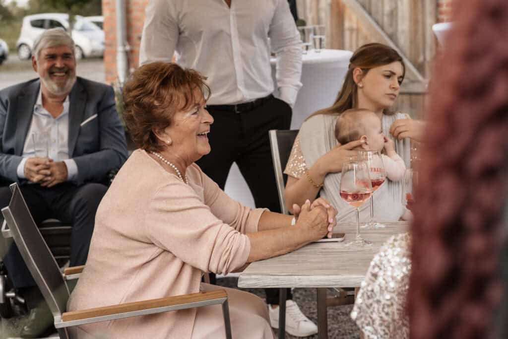 Familienfeier mit lachender älterer Frau und Baby bei Hochzeit oder Event.
