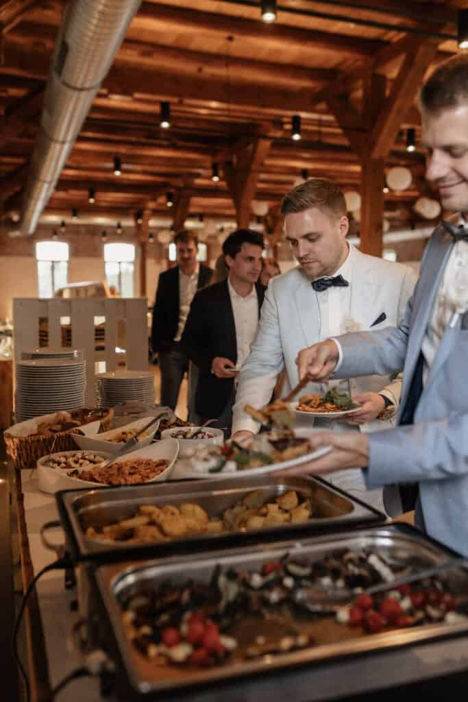 Hochzeitsempfang mit Buffet und Gästen in einem rustikalen Saal.