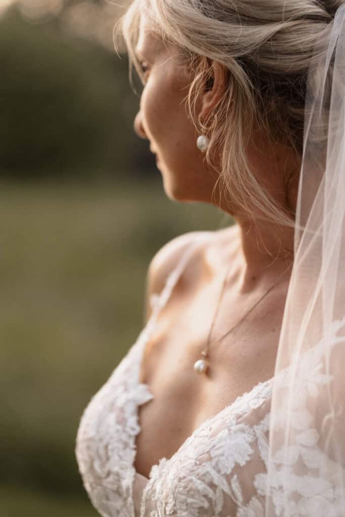 Braut mit Perlenohrringen und Spitzenkleid bei Sonnenuntergang.