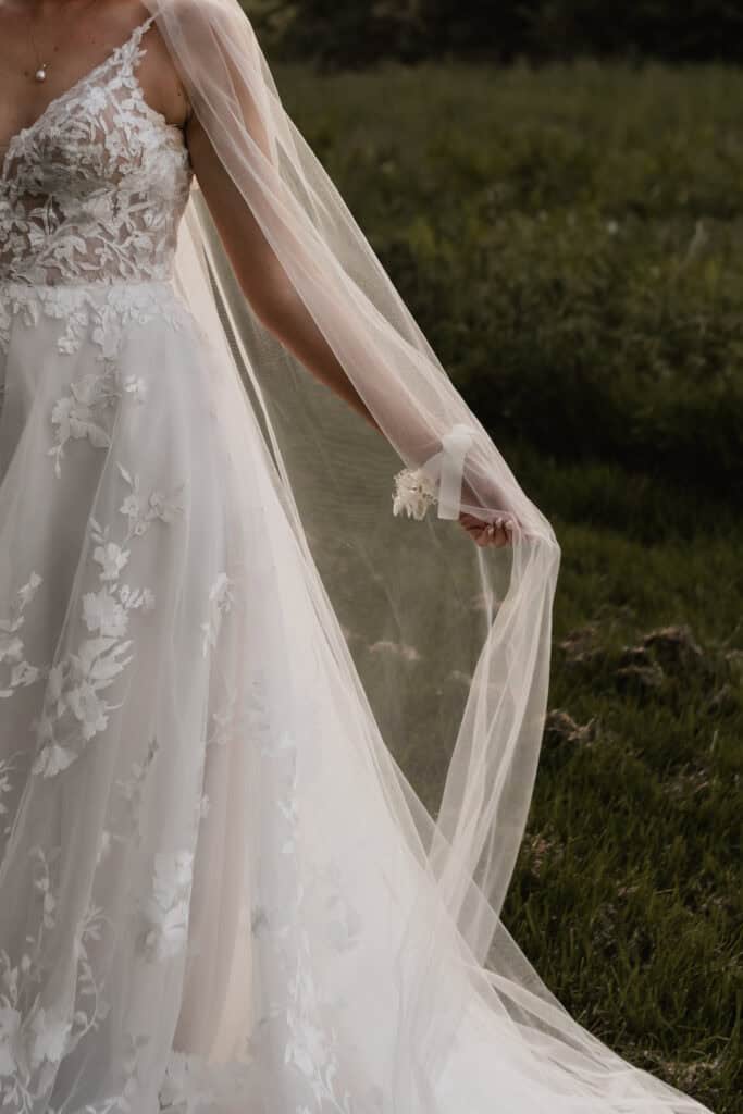Elegantes Hochzeitskleid mit Spitzen-Details und Tüllschleier im Freien.