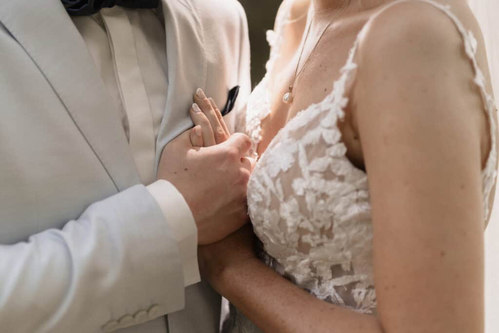 Nahaufnahme eines Brautpaares bei der Hochzeit, Fokus auf Hände und Kleidung.