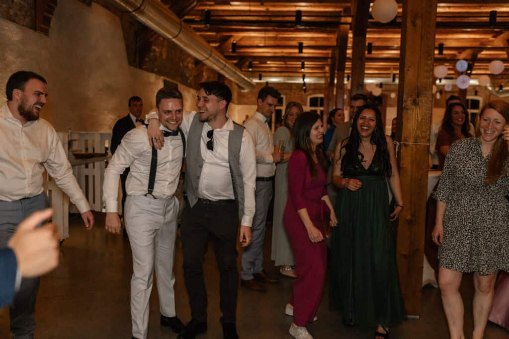 Freudiges Hochzeitsfest mit lachenden Gästen und Tanz in rustikalem Ambiente.