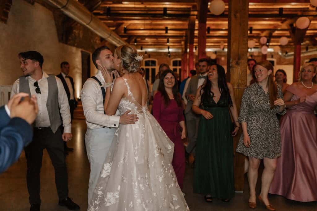 Brautpaar tanzt bei Hochzeit mit Gästen in rustikalem Ambiente.