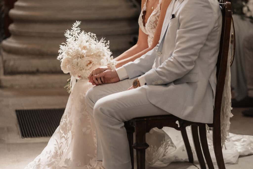 Hochzeitspaar bei der Trauung, Fokus auf Hände und Brautstrauß.