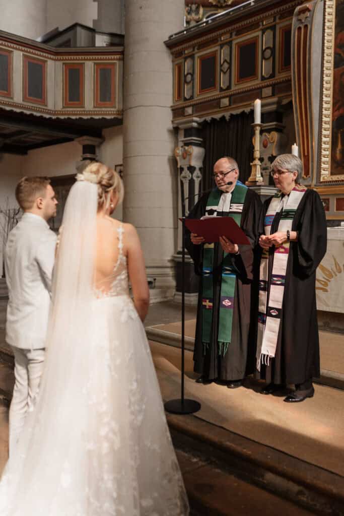 Hochzeitspaar bei der Trauung in der Kirche mit Pfarrer und Pfarrerin.