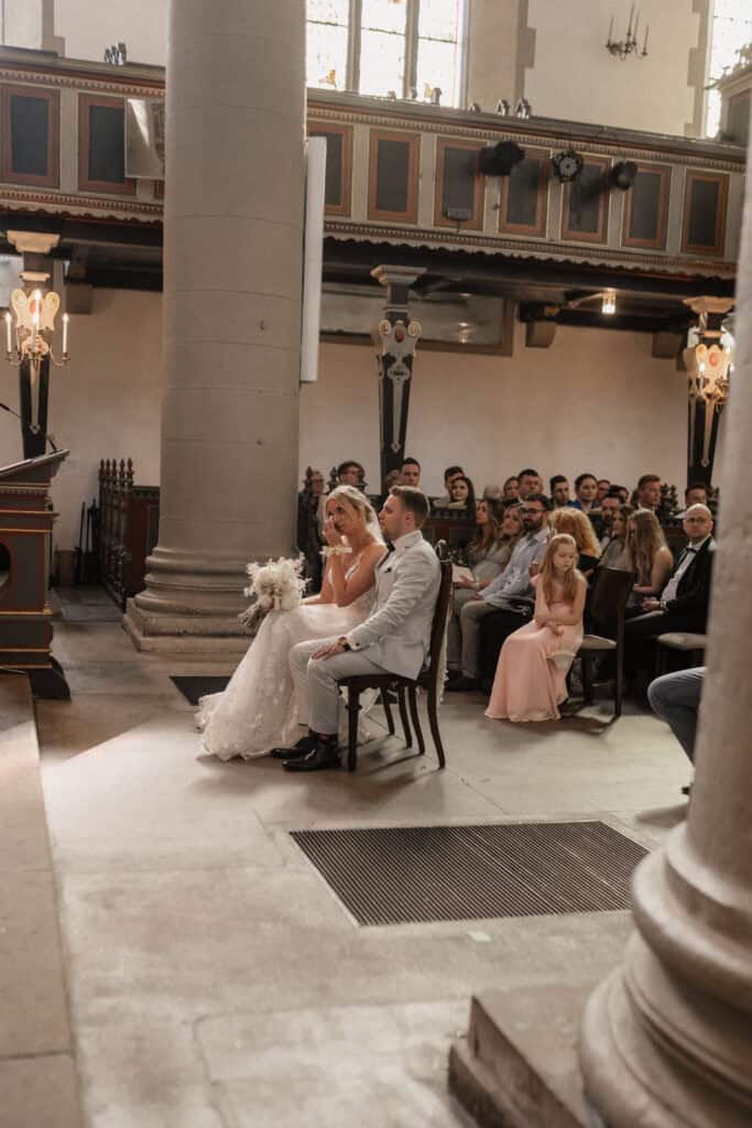 Hochzeitsszene in Kirche mit Braut, Bräutigam und Gästen.
