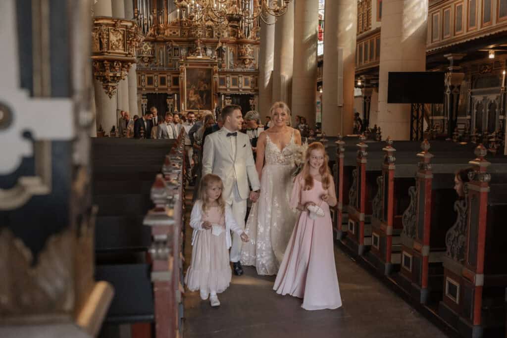 Hochzeit in einer prunkvollen Kirche mit Braut, Bräutigam und zwei Mädchen.
