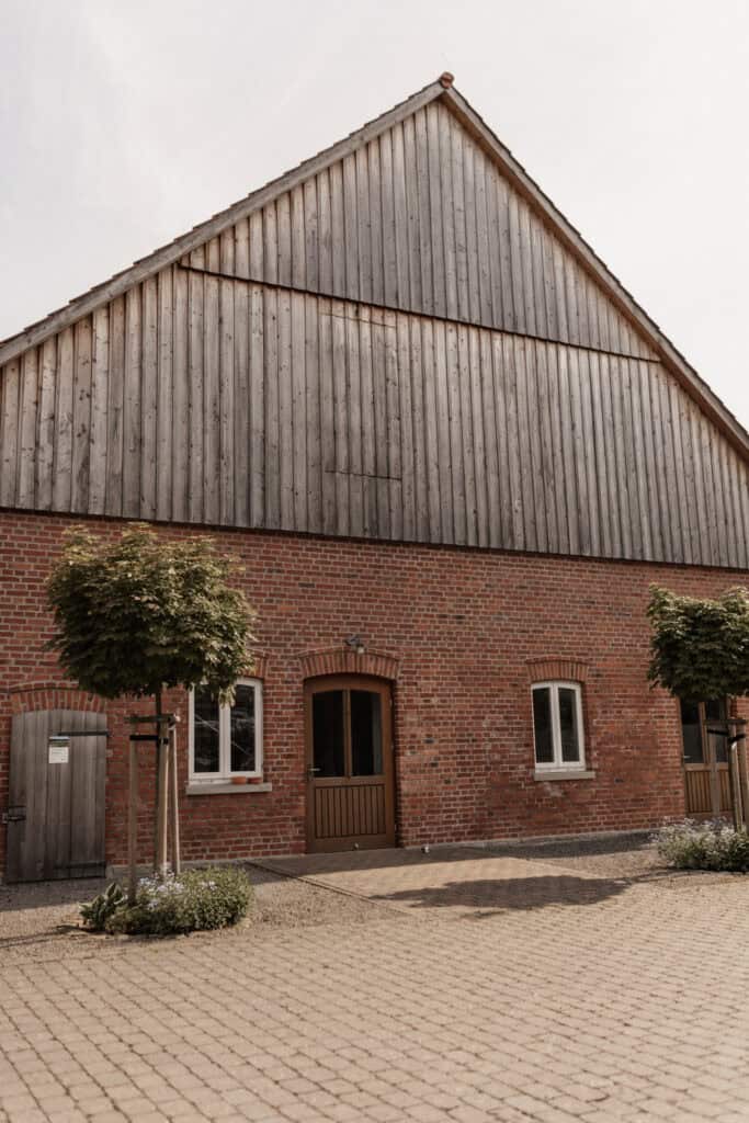 Historisches Bauernhaus mit Holzdach und kleinen Bäumen vor dem Eingang.
