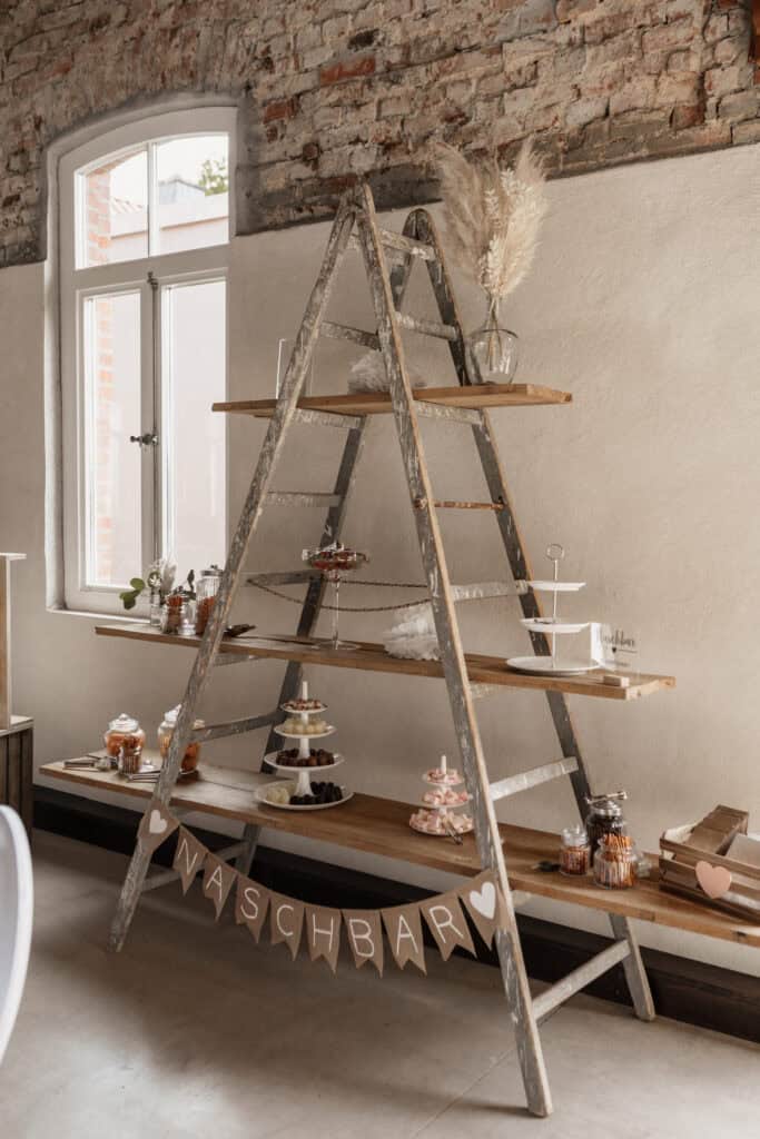 Hochzeitstafel mit Kuchen und Dekorationen auf einer Leiter in rustikalem Raum.