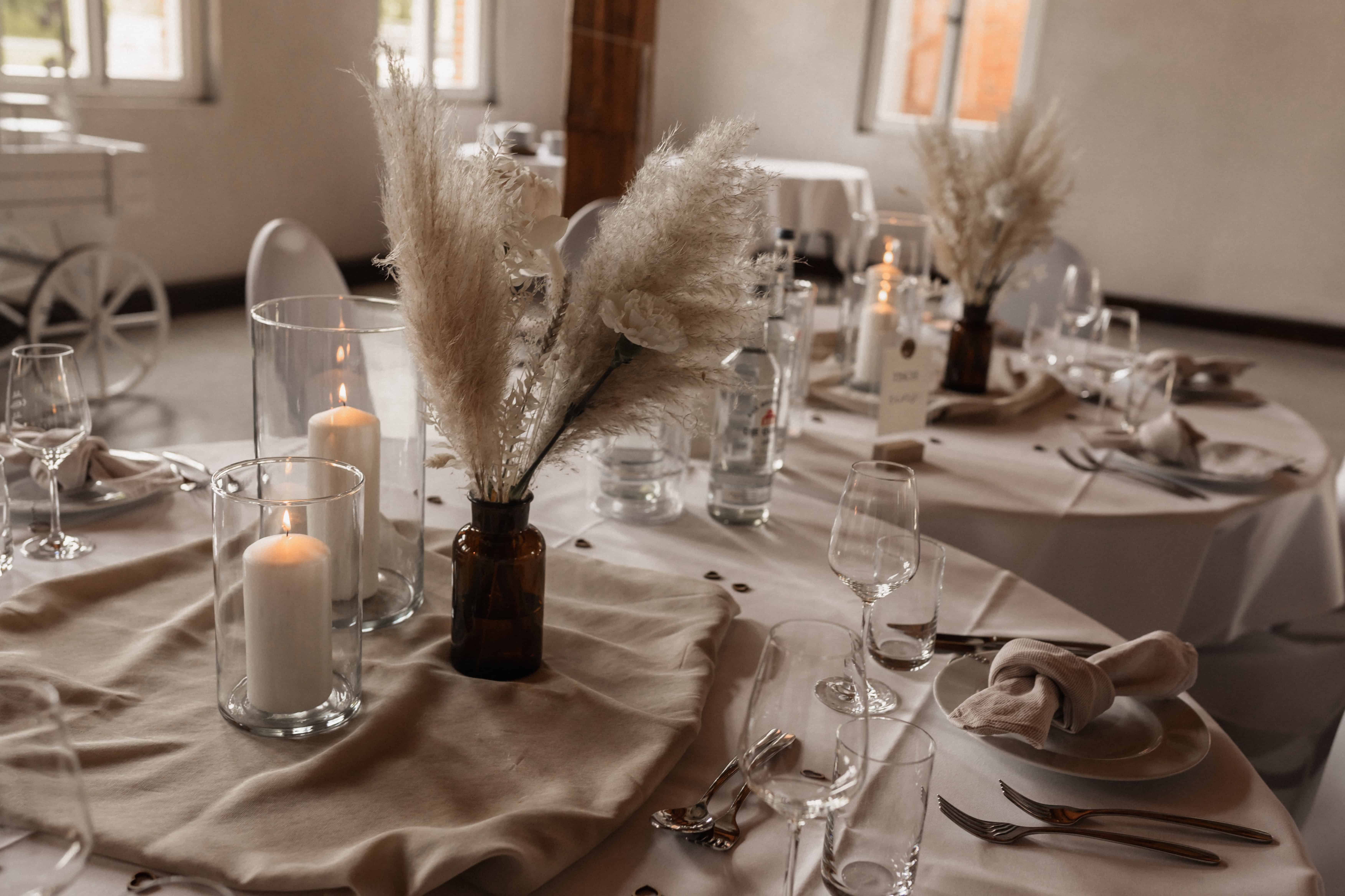 Elegante Tafeldekoration mit Kerzen und Pampasgras in einem Hochzeitsraum.