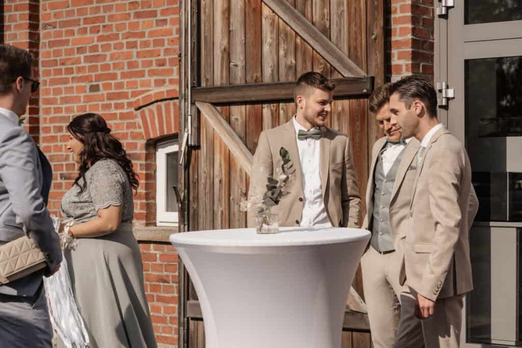 Hochzeitspaar und Gäste bei einer Feier im Freien vor einer alten Scheune.